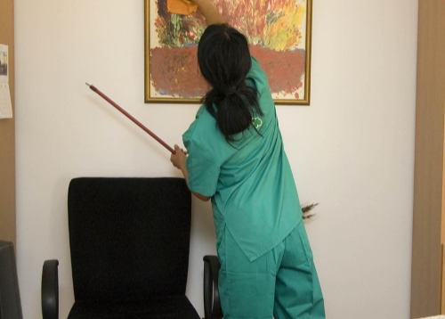 uniformed Person cleaning a painting on a wall in an office setting