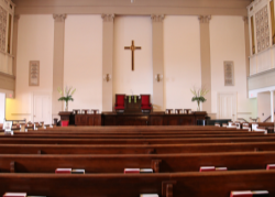 Empty church interior with wooden pews and a cross on the wall.