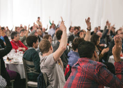 People at a conference or event with raised hands, indicating participation or agreement.